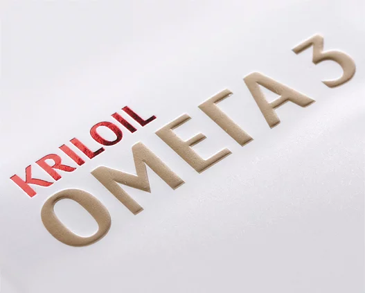 Текст на белой поверхности гласит: «KRILOIL» красным цветом и «ОМЕГА 3» (Omega 3 кириллицей) рельефными бежевыми буквами, среди которых указано название Soldis.