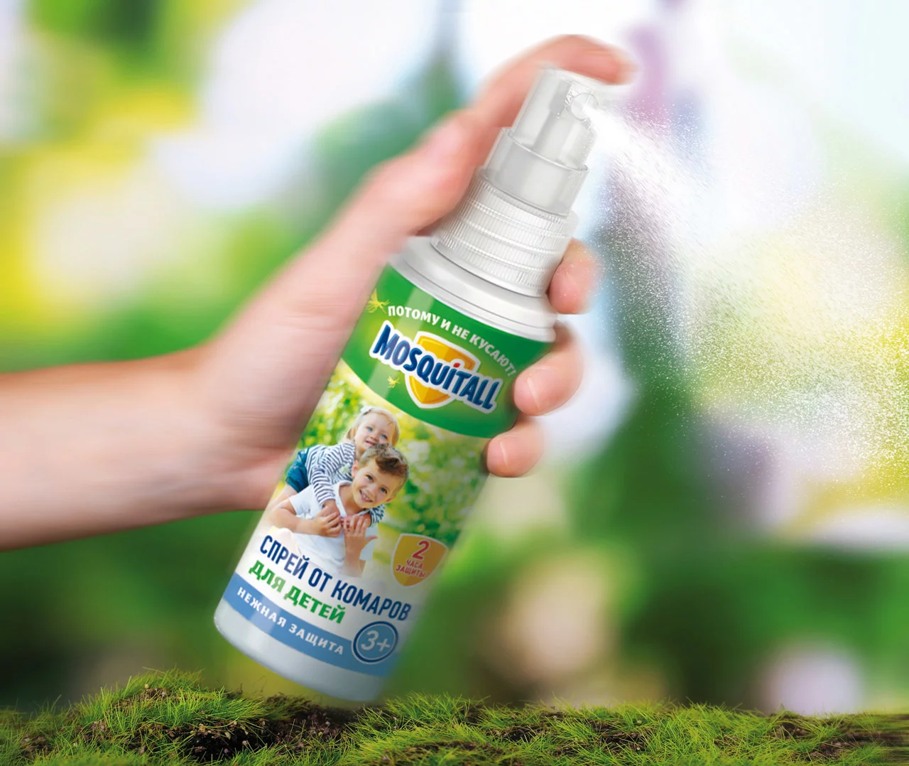 Рука распыляет средство от комаров MOSQUITALL для детей, произведенное Soldis. На баллончике изображены два улыбающихся ребенка и текст на русском языке. Зеленый размытый фон намекает на обстановку на открытом воздухе.