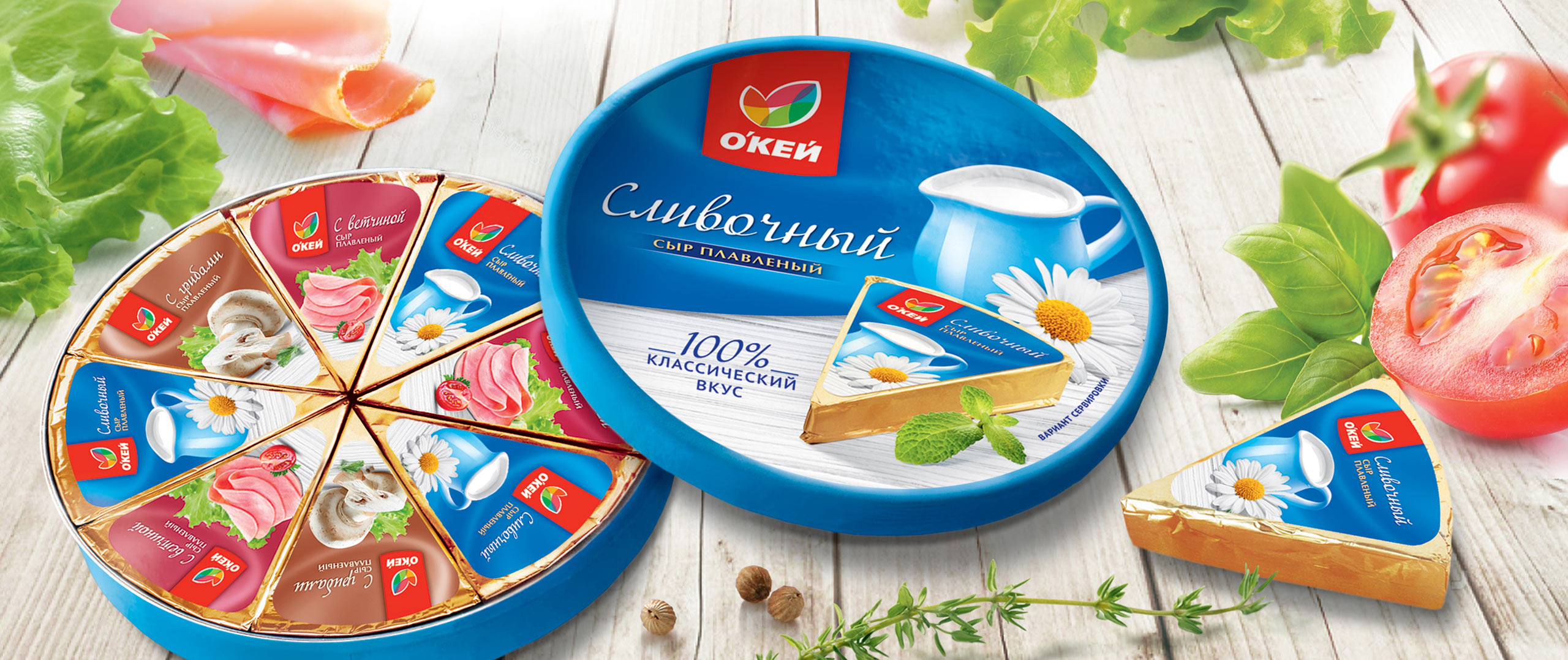 Круглая коробка плавленых сырков Soldis Russian открыта, показывая отдельные кусочки в сине-золотой обертке. Свежие овощи, зелень и нарезанные помидоры разложены вокруг коробки на деревянной поверхности.