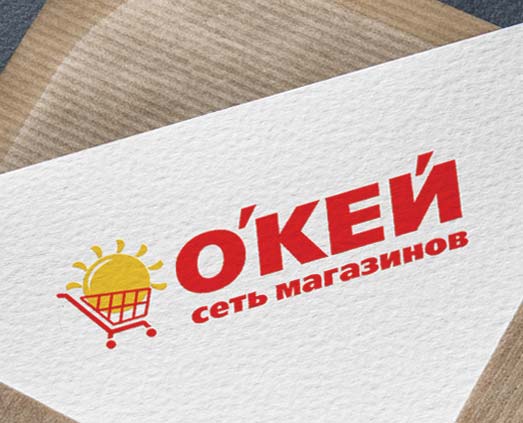 Логотип с изображением красной тележки для покупок, держащей желтое солнце, рядом с жирными красными словами кириллицы ОКЕЙ сеть магазинов, представляющими сеть магазинов OKEY, созданный Soldis на белой текстурированной поверхности.