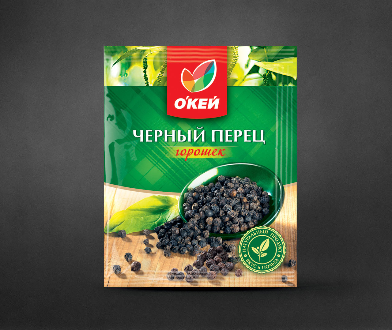 Зелено-желтая упаковка черного перца марки OKEY, на которой изображены горошины перца Soldis, высыпающиеся из черной миски на деревянную поверхность, с текстом на русском языке и логотипом в виде зеленого листа на лицевой стороне.