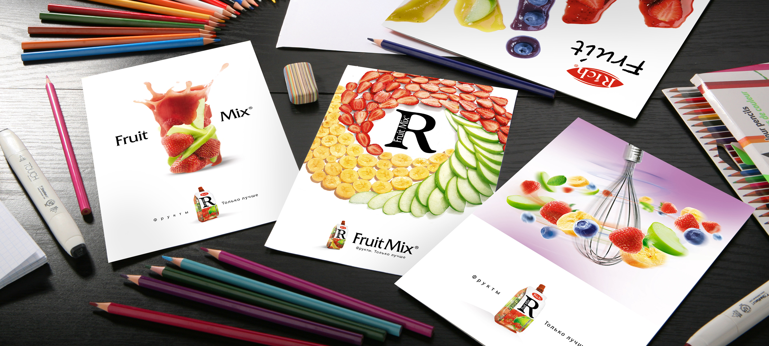 Четыре листовки Fruit Mix с красочными фруктовыми рисунками разложены на столе среди цветных карандашей, маркеров, ластика и листов бумаги. На каждой листовке изображен логотип Fruit Mix и креативные фруктовые рисунки Солдиса.