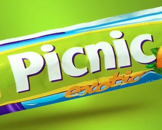 Крупный план обертки шоколадного батончика Picnic Exotic от Soldis с ярким белым и фиолетовым текстом на зеленом фоне и намеком на изображение оранжевого фрукта с правой стороны.