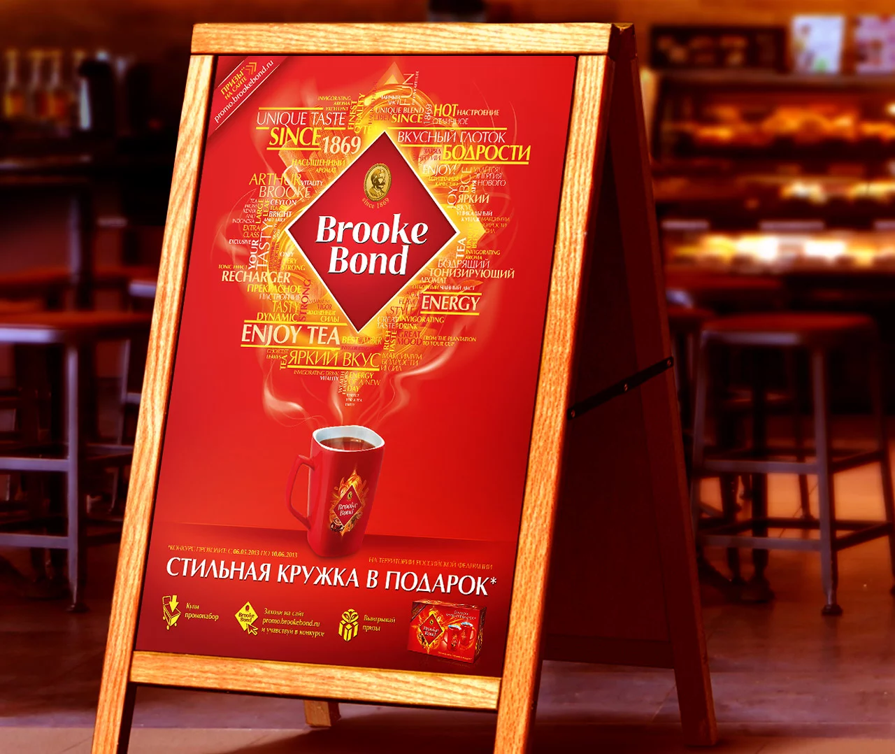 На деревянном мольберте висит красный рекламный плакат Soldis для чая Brooke Bond, на котором изображена дымящаяся чашка и золотой текст на русском языке в уютном кафе с размытым светом и выпечкой на заднем плане.